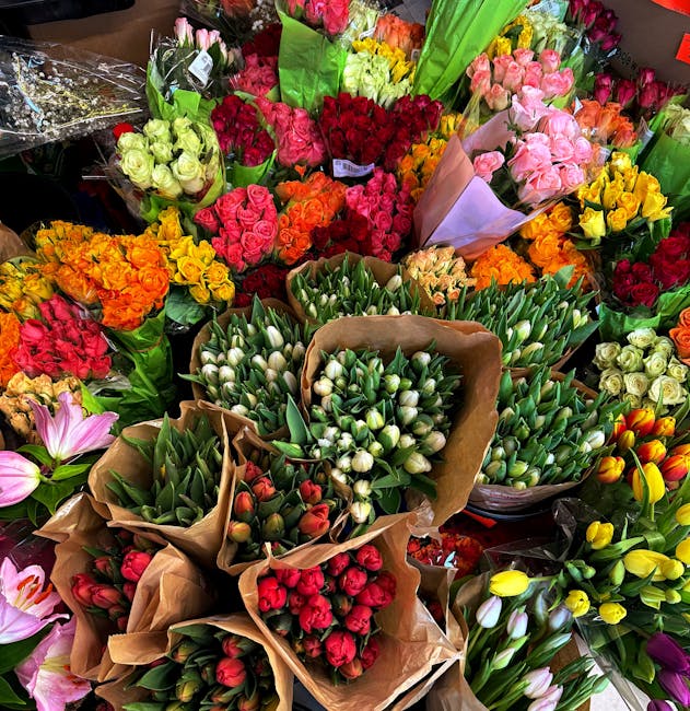 A vibrant display of fresh floral arrangements featuring a variety of flowers such as roses, tulips, and hyacinths in colors including red, pink, yellow, orange, and white. The flowers are wrapped in