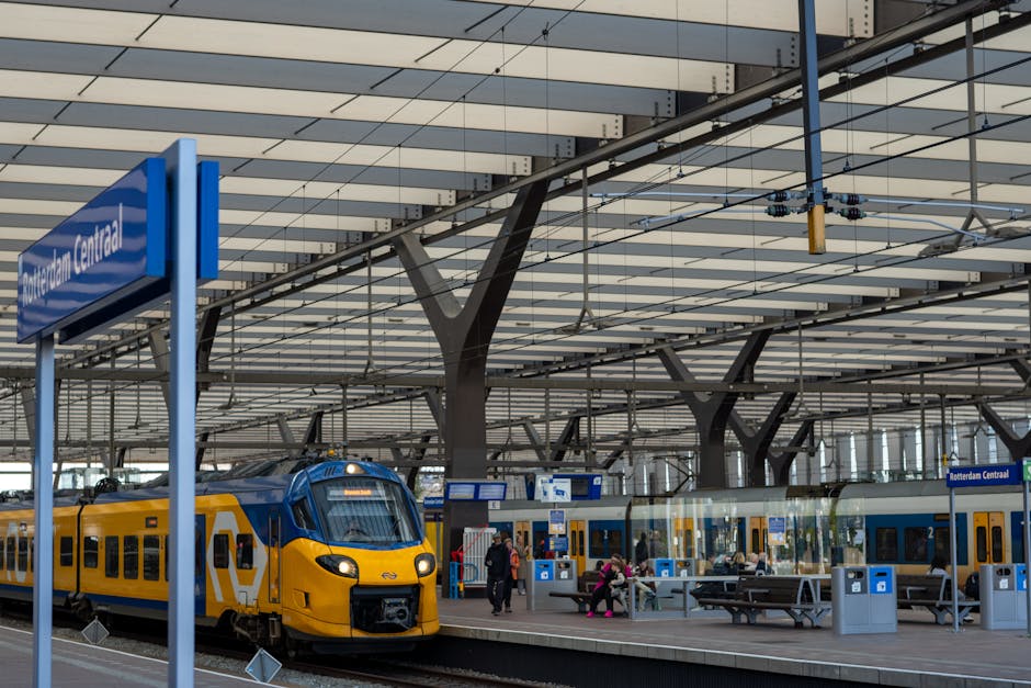 Interior view of Rotterdam Central train station featuring a modern architectural design with a high, multi-layered ceiling supported by black structural beams and numerous parallel white panels. A br